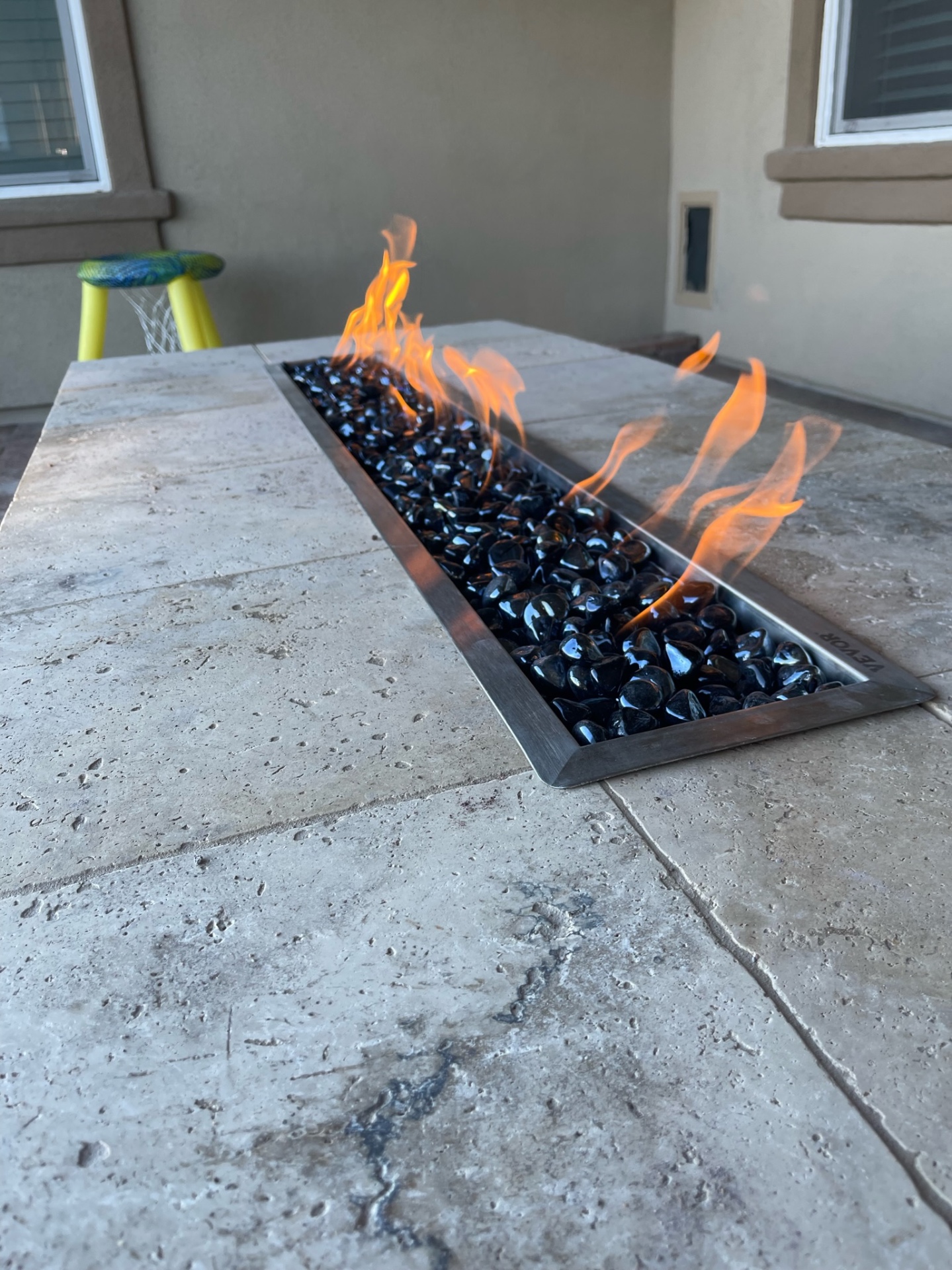 Peoria linear gas fire feature with black fire glass set into travertine paver bar top on stamped concrete patio by AE Outdoor Living
