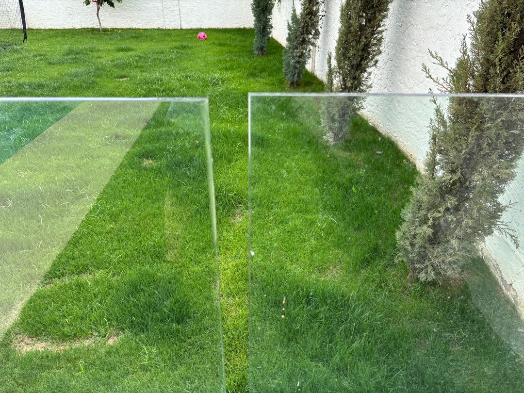 Vertical joint between glass barrier panels with visible variation in gap width along a lawn edge.