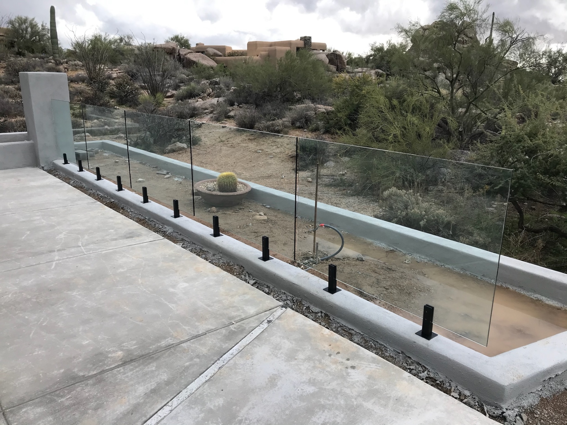 Straight run of frameless tempered glass panels along a Sonoran Desert pool deck with saguaros and Pueblo-style homes in the distance.