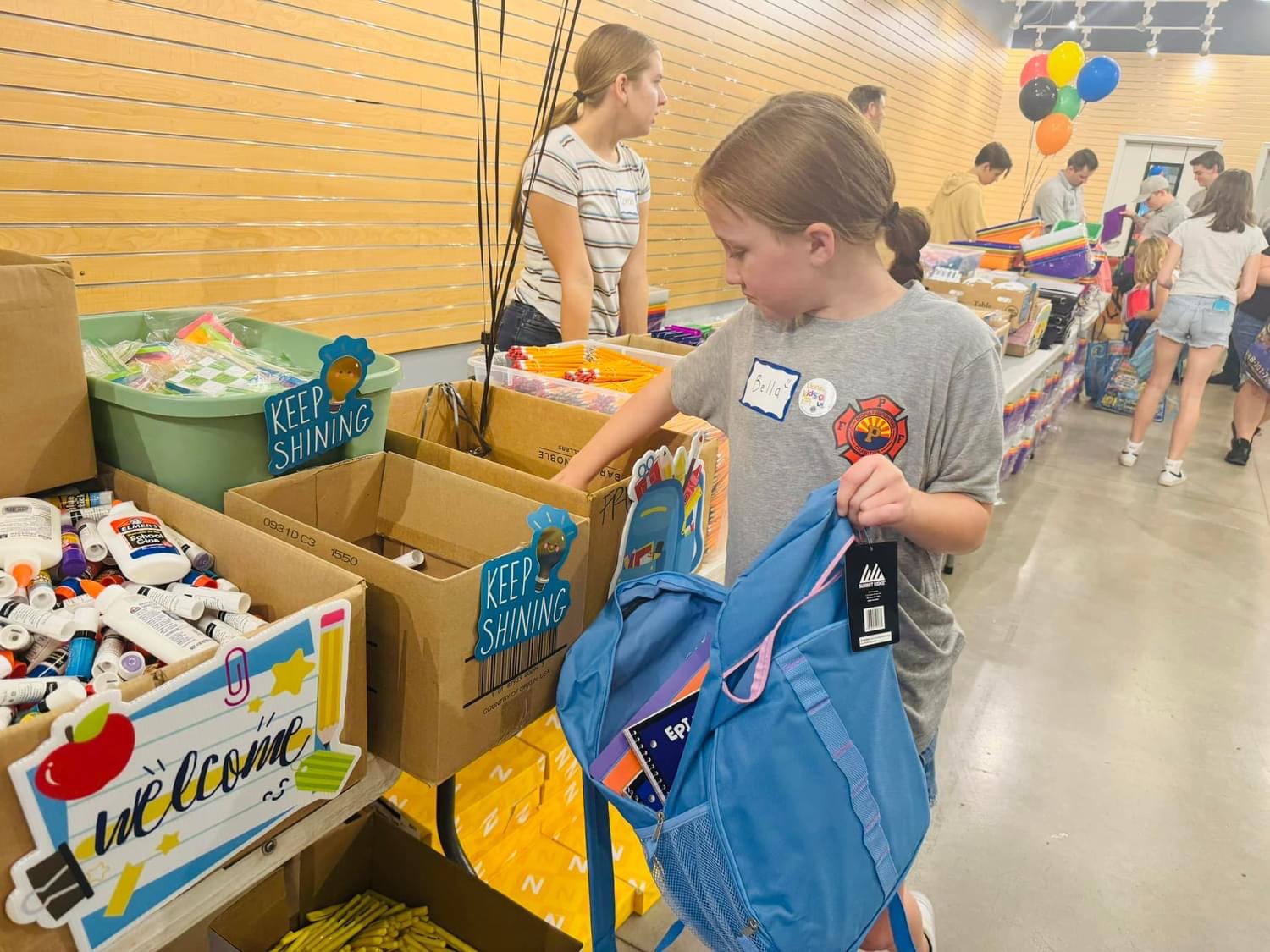 Young girl wearing a Peoria Fire-Medical shirt picking out a blue backpack and supplies at the giveaway