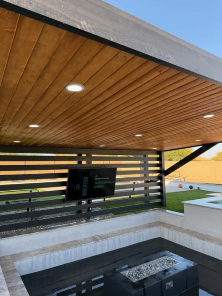 Black pergola with wood slat ceiling and integrated TV wall over outdoor living zone