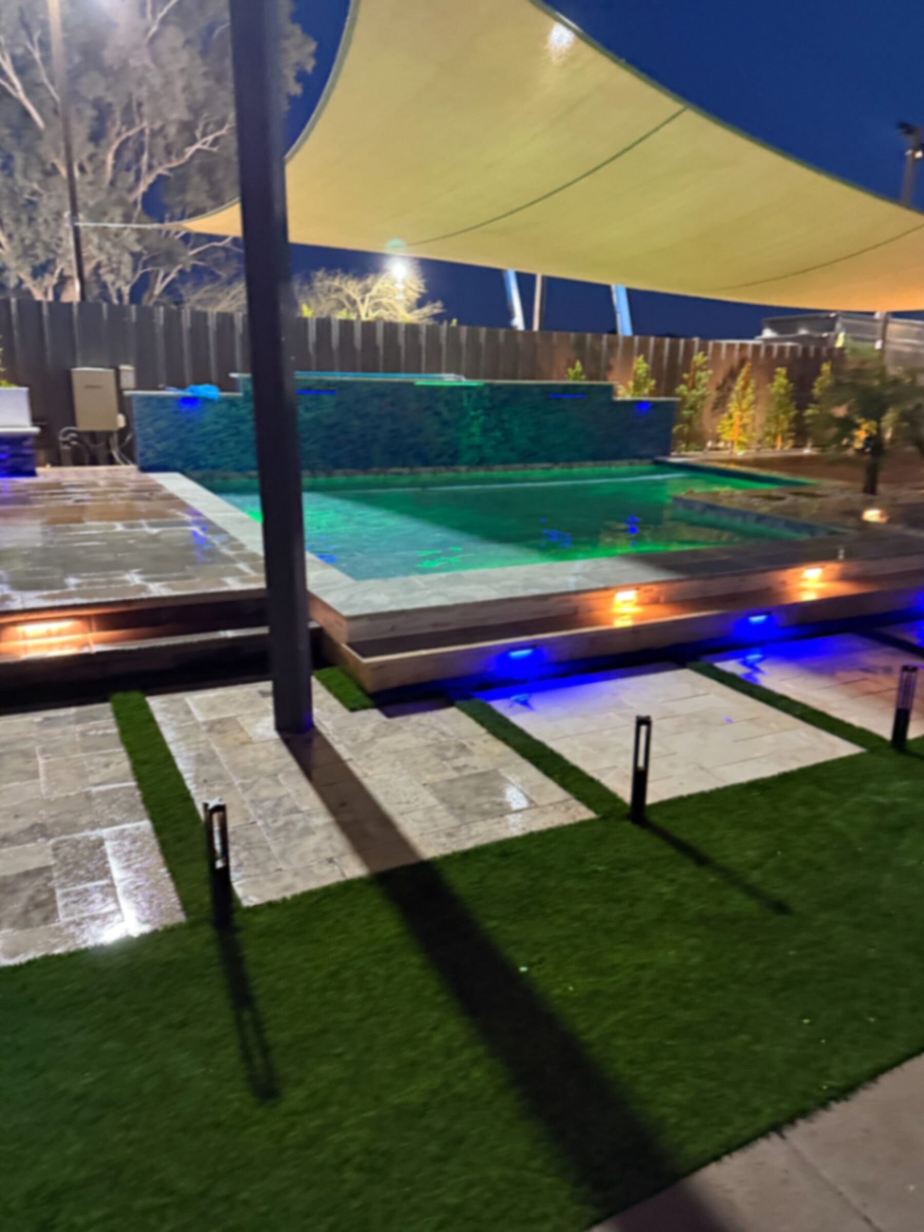Display pool seen from under the pergola with shade sail overhead and full color LED lighting active