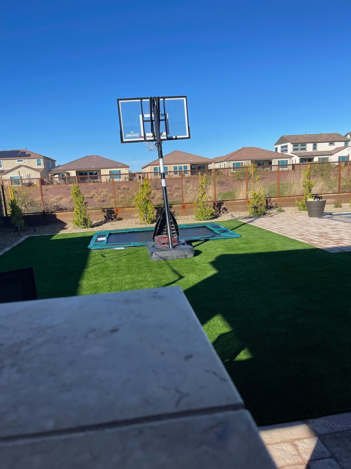 Peoria backyard artificial turf sport lawn with in-ground trampoline and portable basketball hoop bordered by paver patio