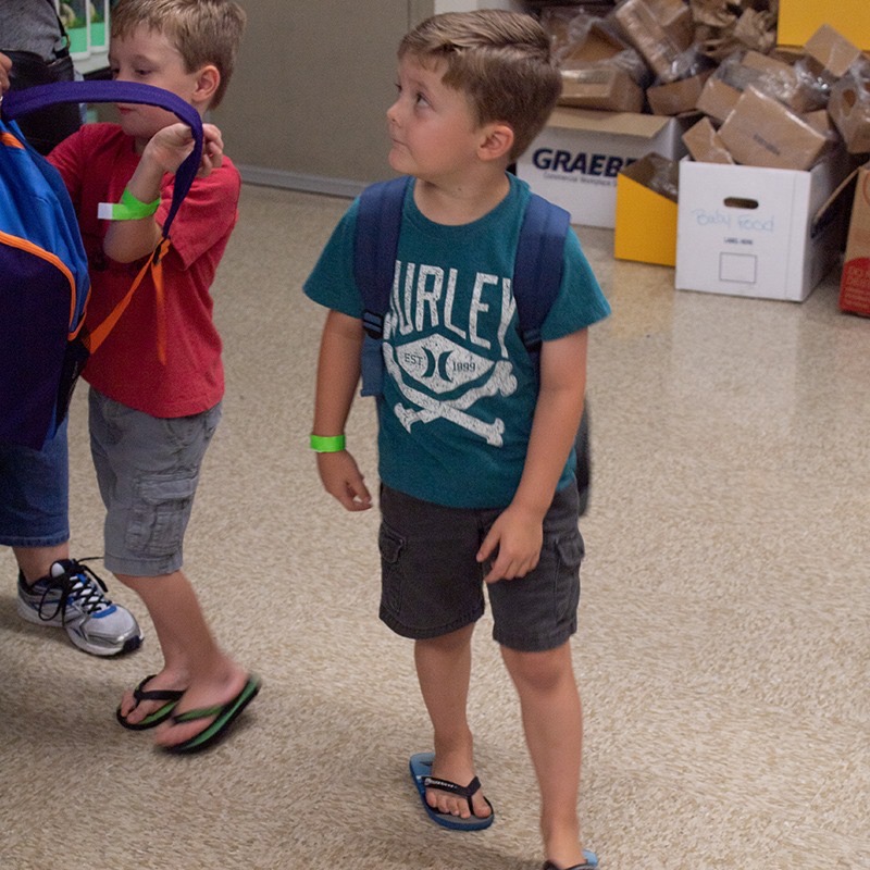 Two young boys trying on new backpacks after picking them out at the drive