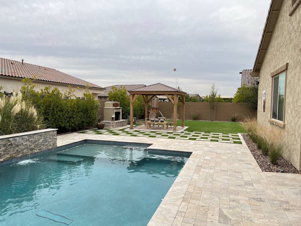 Vask residence The Meadows Peoria AZ full-yard view with pool spillway, checkerboard turf-and-travertine transition, cedar gazebo, and stucco outdoor fireplace