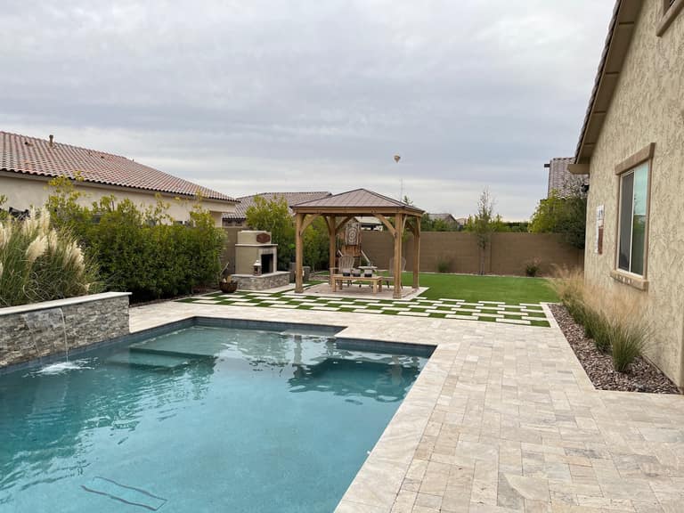 Vask residence The Meadows Peoria AZ full-yard view with pool spillway, checkerboard turf-and-travertine transition, cedar gazebo, and stucco outdoor fireplace