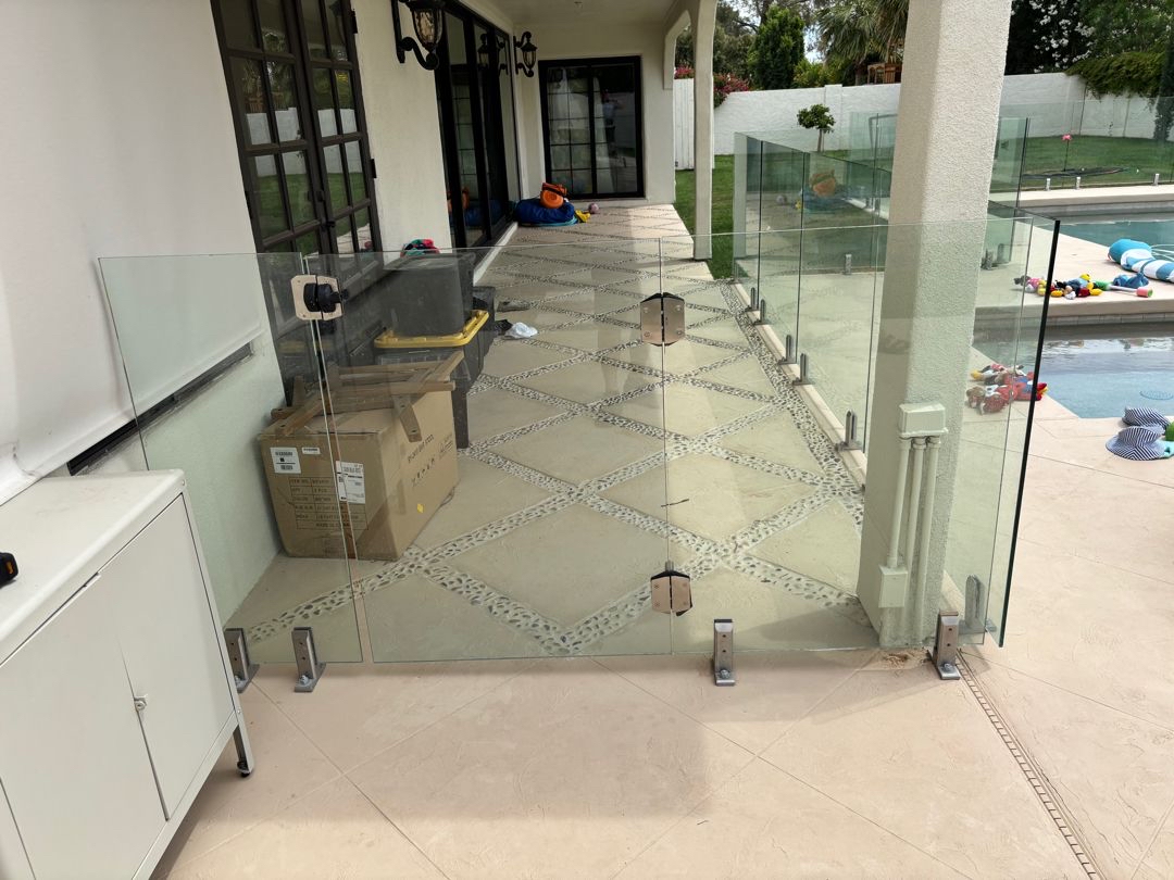 Site photo showing a hardware box, suction cup and base-plate spigots staged on the deck near a glass pool barrier.
