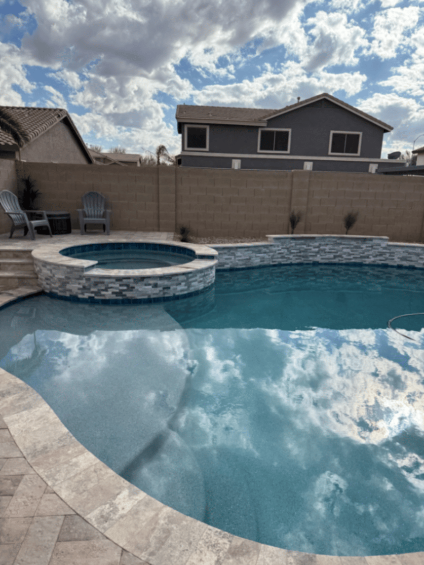 Raised spa and freeform pool with tile band and light stone deck in an Arizona backyard