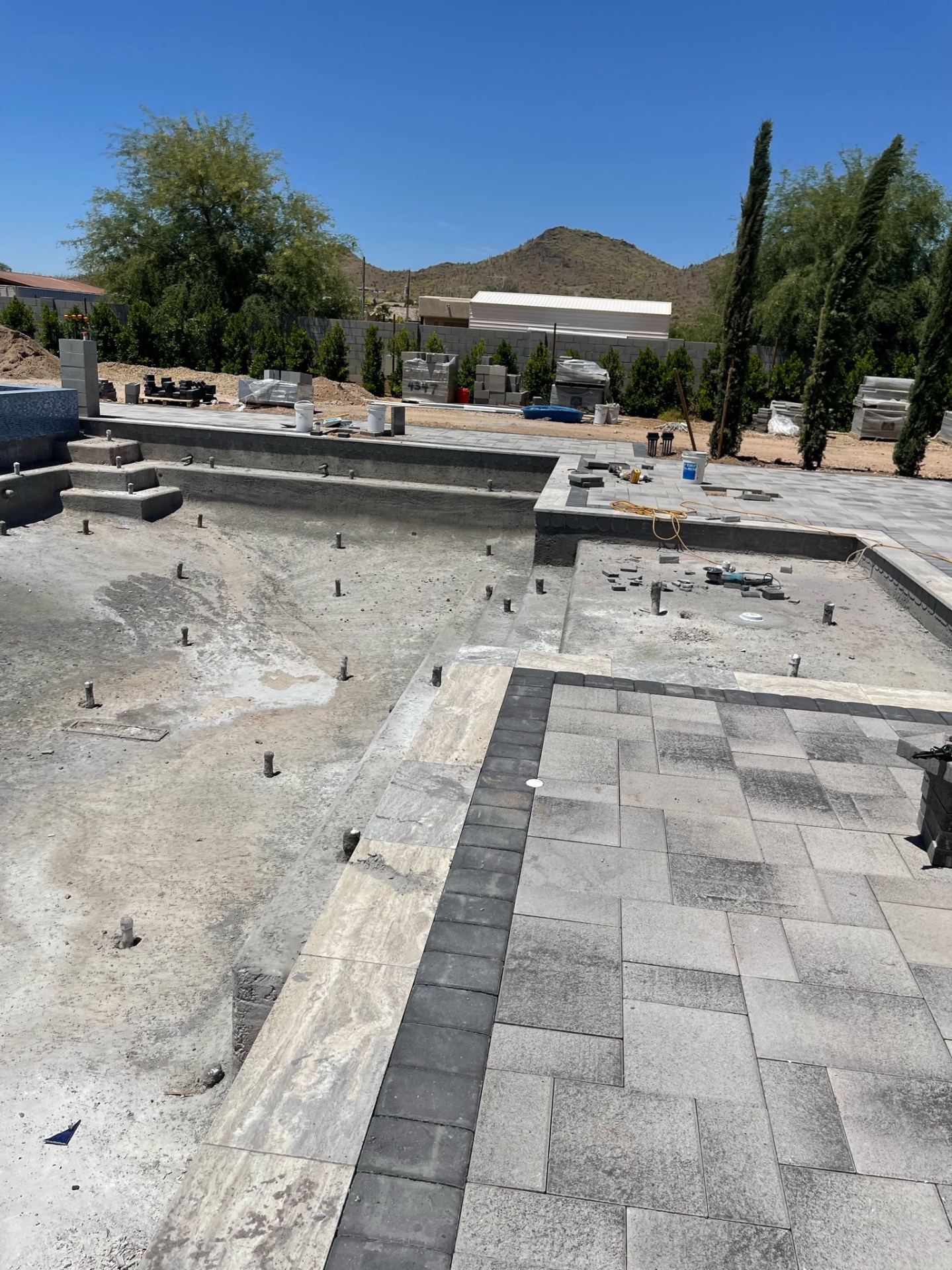 Wide poolside view with near-finished large-format paver deck, coping, and clean lines stretching toward the back wall