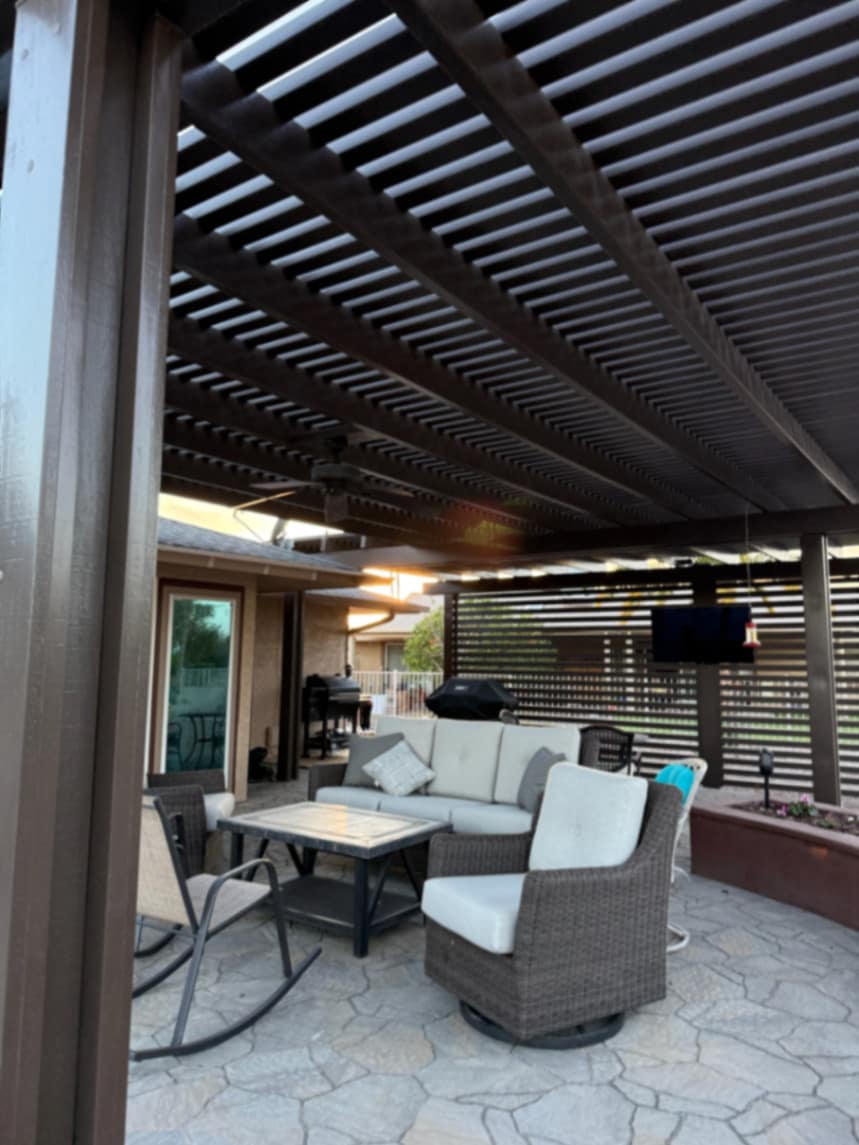 Thorn residence Mesa AZ louvered black aluminum pergola with wood slat privacy wall over flagstone-pattern paver patio and wicker lounge set at dusk