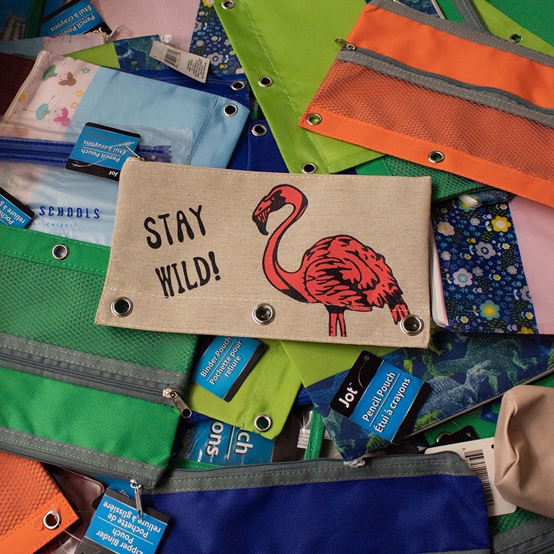 Pile of colorful zipper pencil pouches including a Stay Wild flamingo pouch ready for distribution