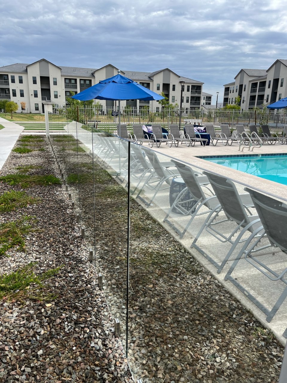 Long run of frameless glass fence panels on metal spigots beside an apartment community pool deck.
