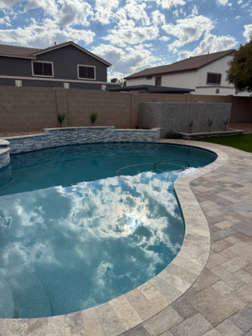 Curved pool waterline reflecting a cloudy Arizona sky against a travertine deck and raised beam.