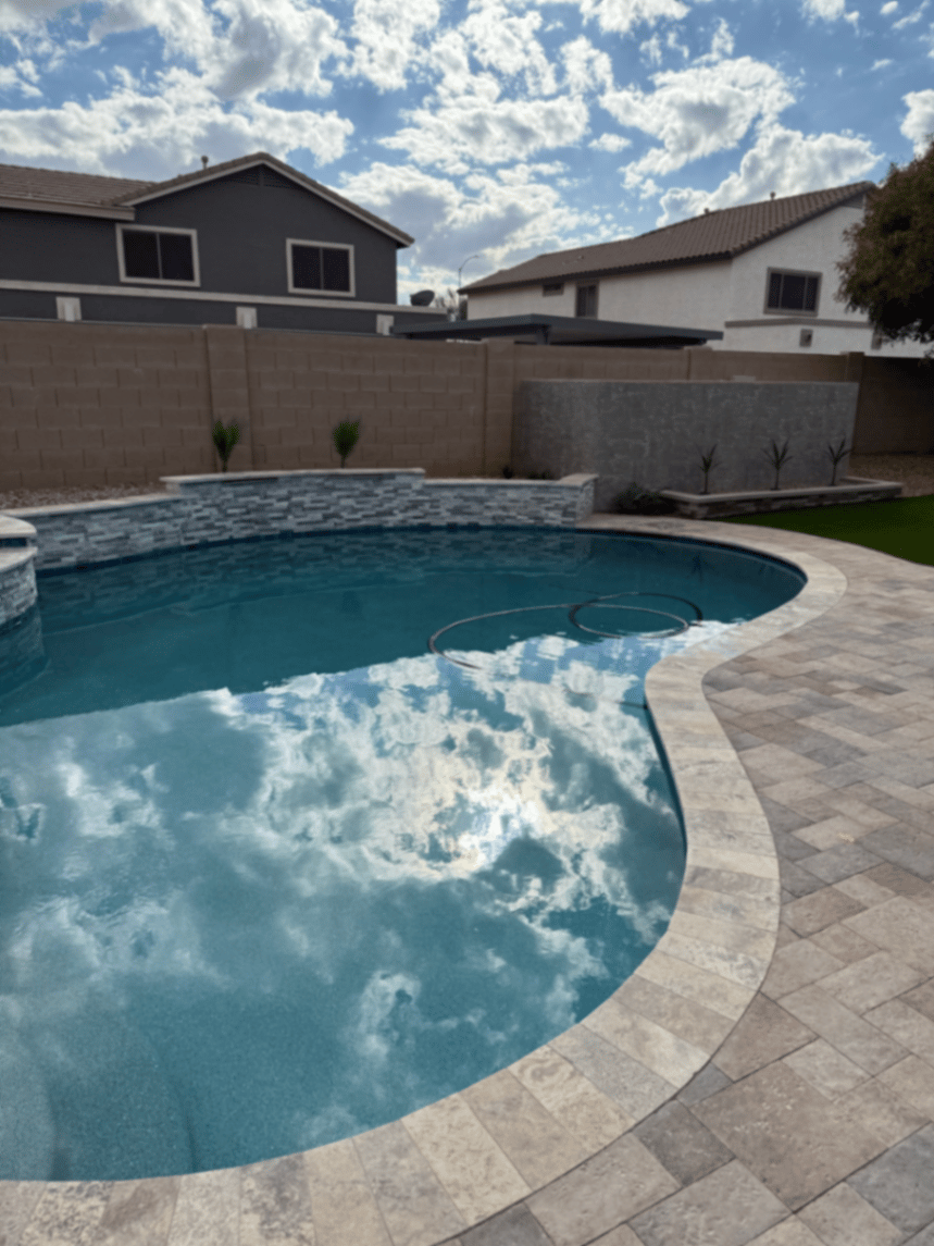 Freeform pool with curved travertine deck and raised beam reflecting clouds in the water
