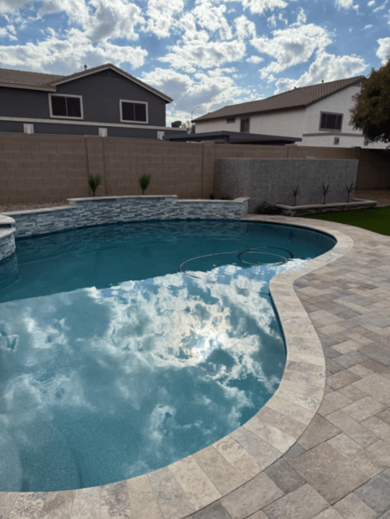 Curved pool waterline reflecting a cloudy Arizona sky against a travertine deck and raised beam.