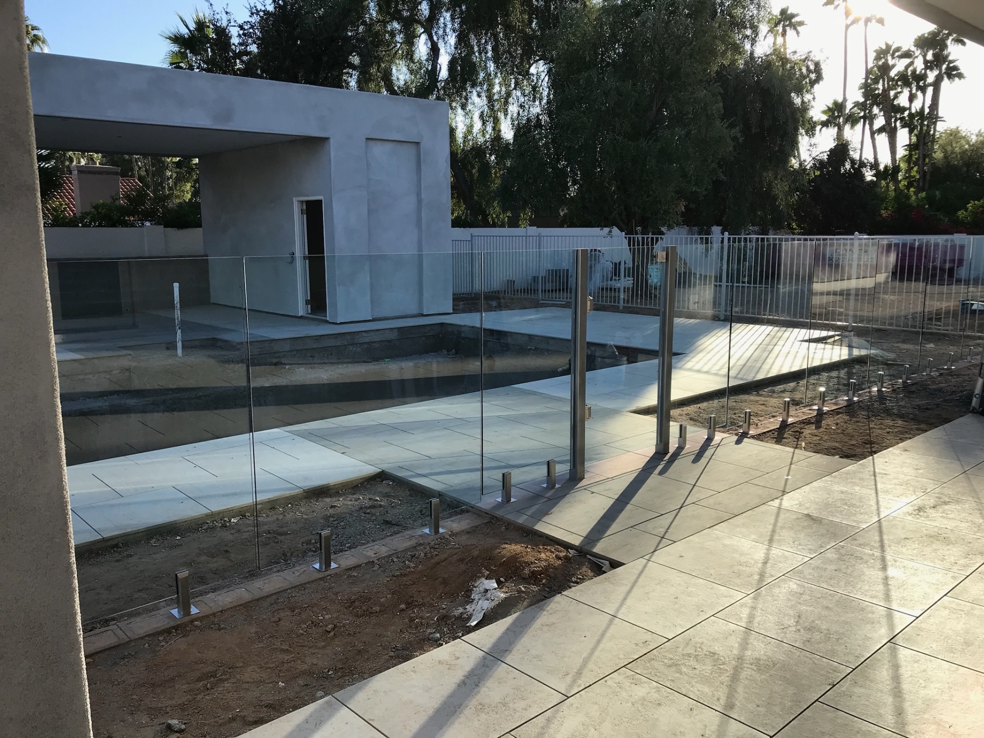 Wide view of a frameless glass pool fence enclosing a new pool, spa, and pavilion with porcelain paver decking and stainless spigot mounts.