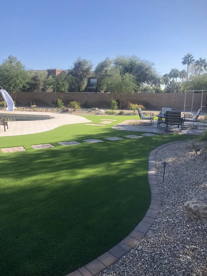 Curved artificial turf, inset paver steps, desert rock and a path light beside a backyard pool in Glendale.