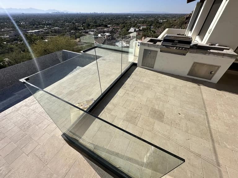 Tiled terrace landing with frameless glass railing next to an outdoor kitchen grill station.