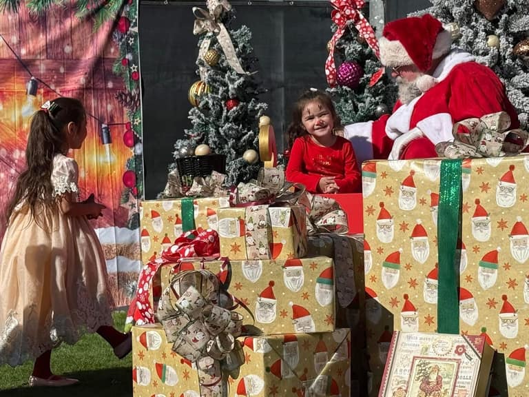 Child visiting Santa next to a stack of wrapped gifts at A Day of Giving 2025