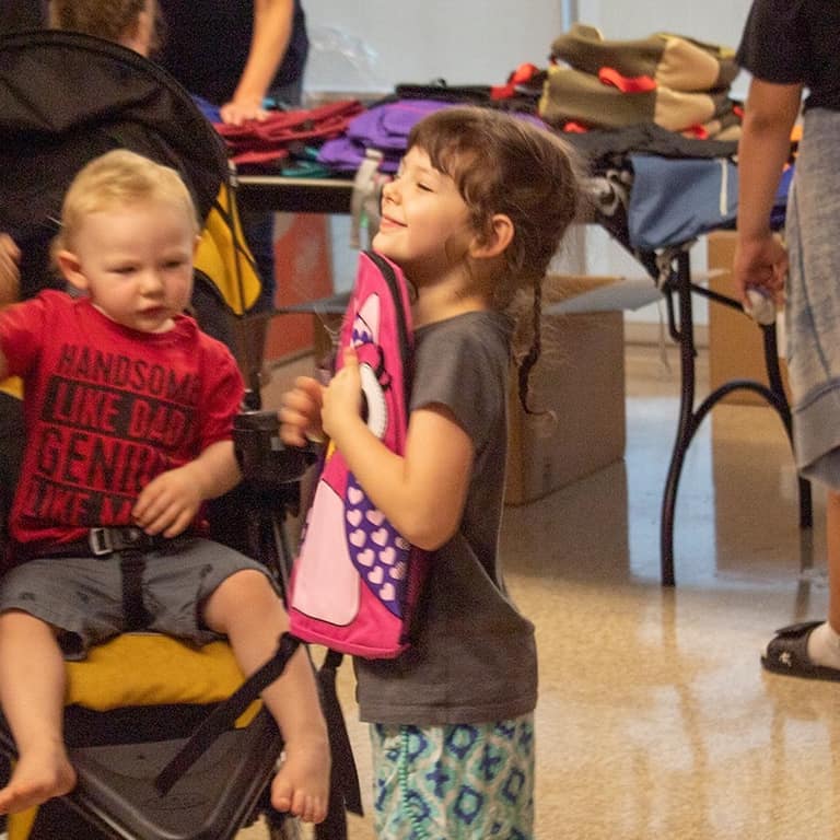 Young girl hugging a pink backpack after receiving it at the backpack drive
