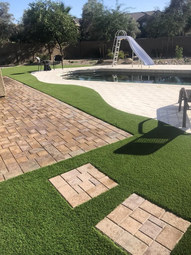 Paver patio and square paver steps integrated with artificial turf beside a backyard pool.