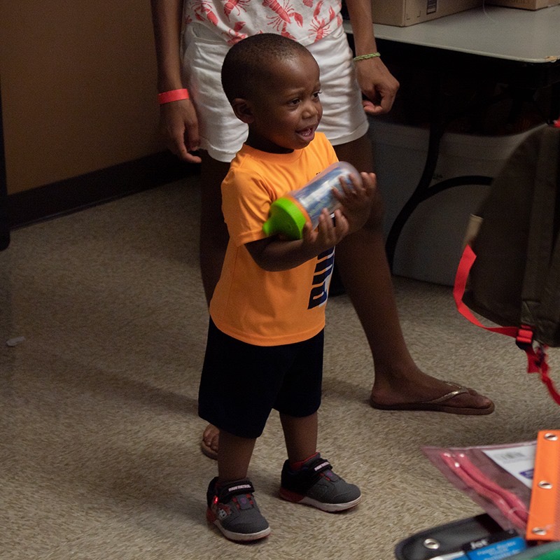 Young boy smiling while holding a school supply bottle during the backpack drive