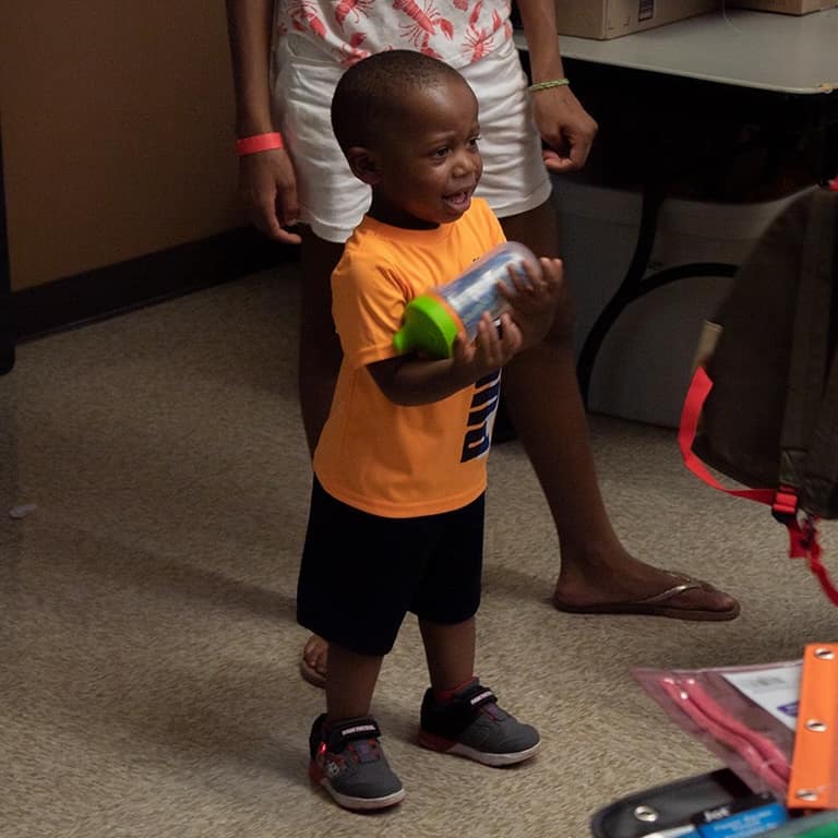 Young boy smiling while holding a school supply bottle during the backpack drive