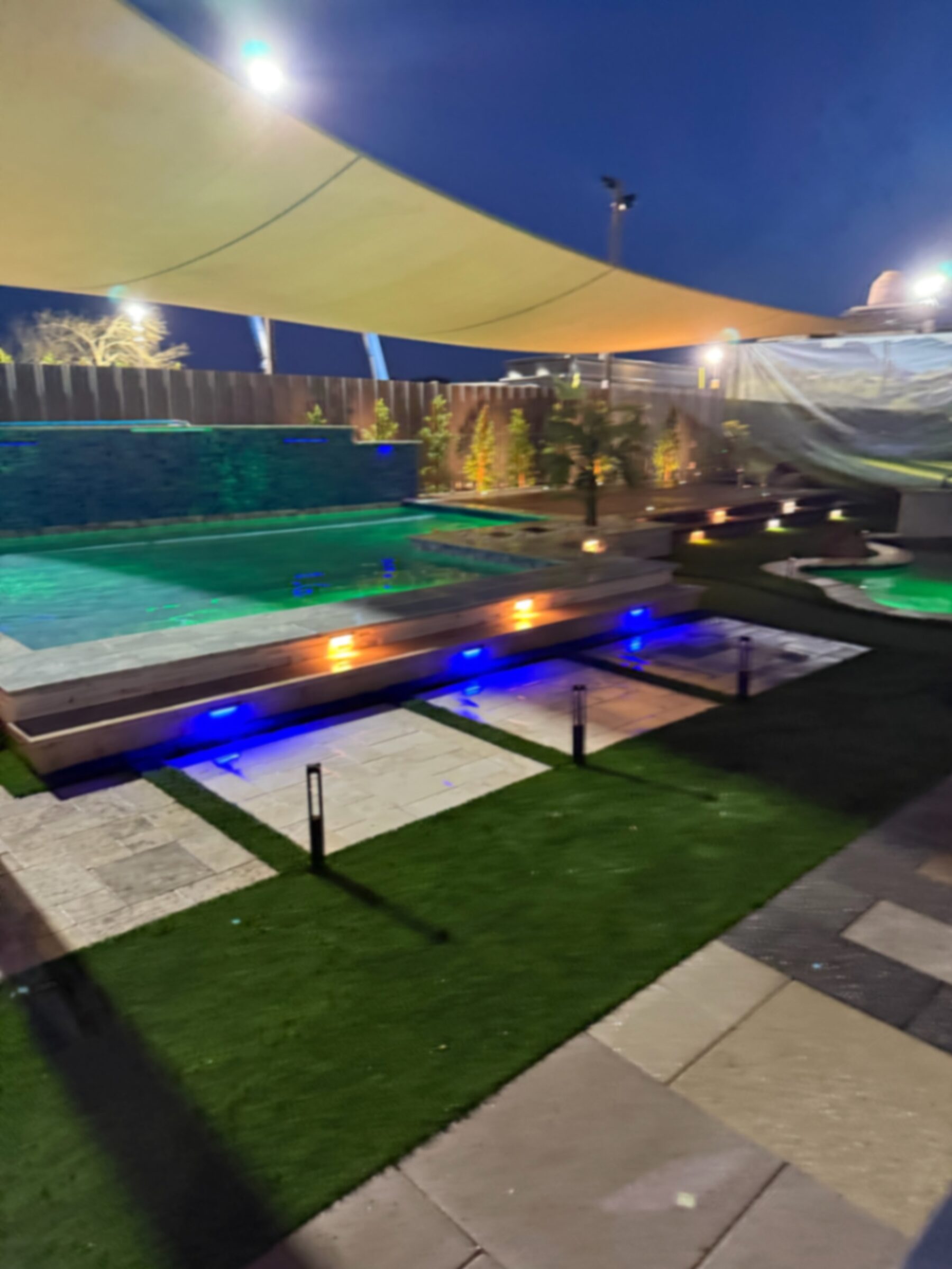 Display pool in green LED mode with blue bench lighting and warm under-coping accents at night