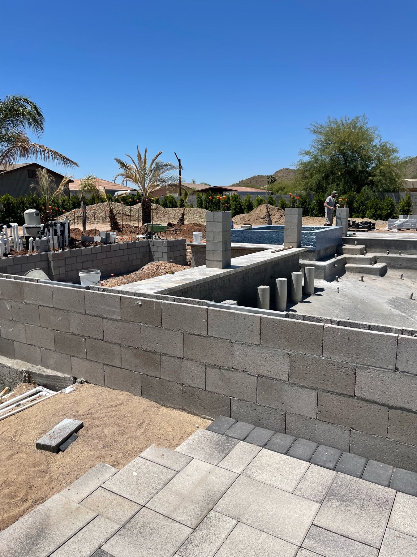 Pool perimeter block walls with raised tiled spa, plumbing manifold, and mason finishing block in background