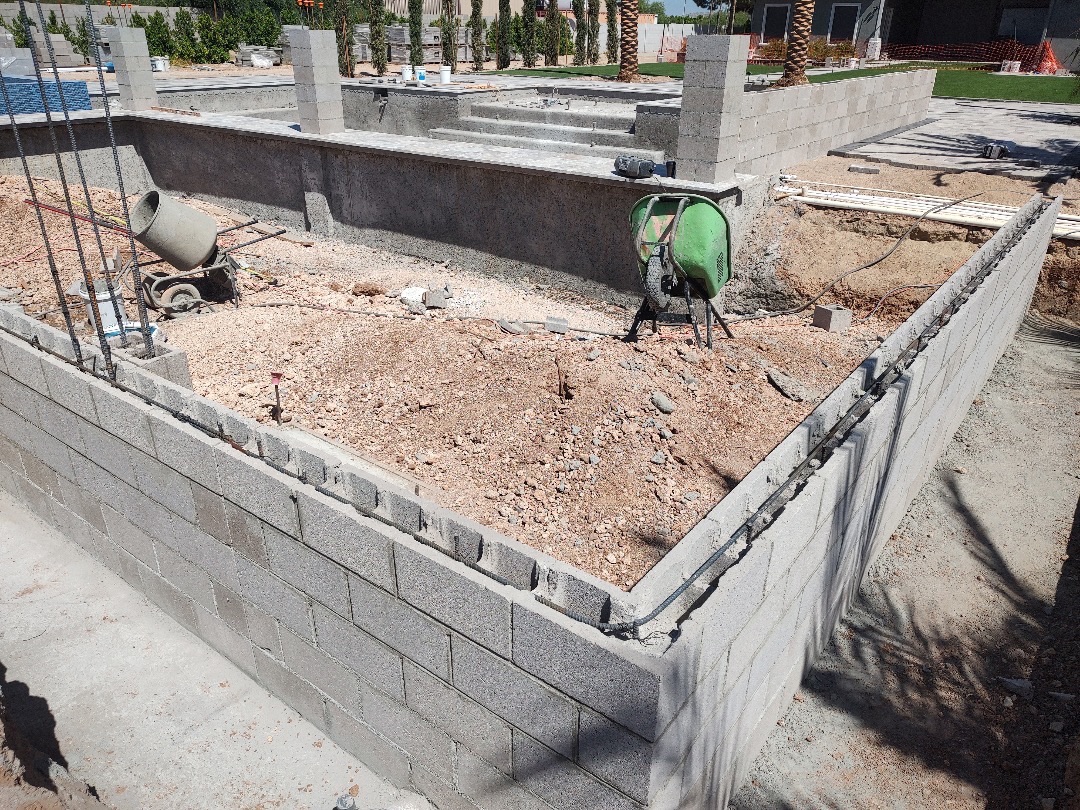 Concrete block enclosure with mixer and wheelbarrow, raised spa visible beyond