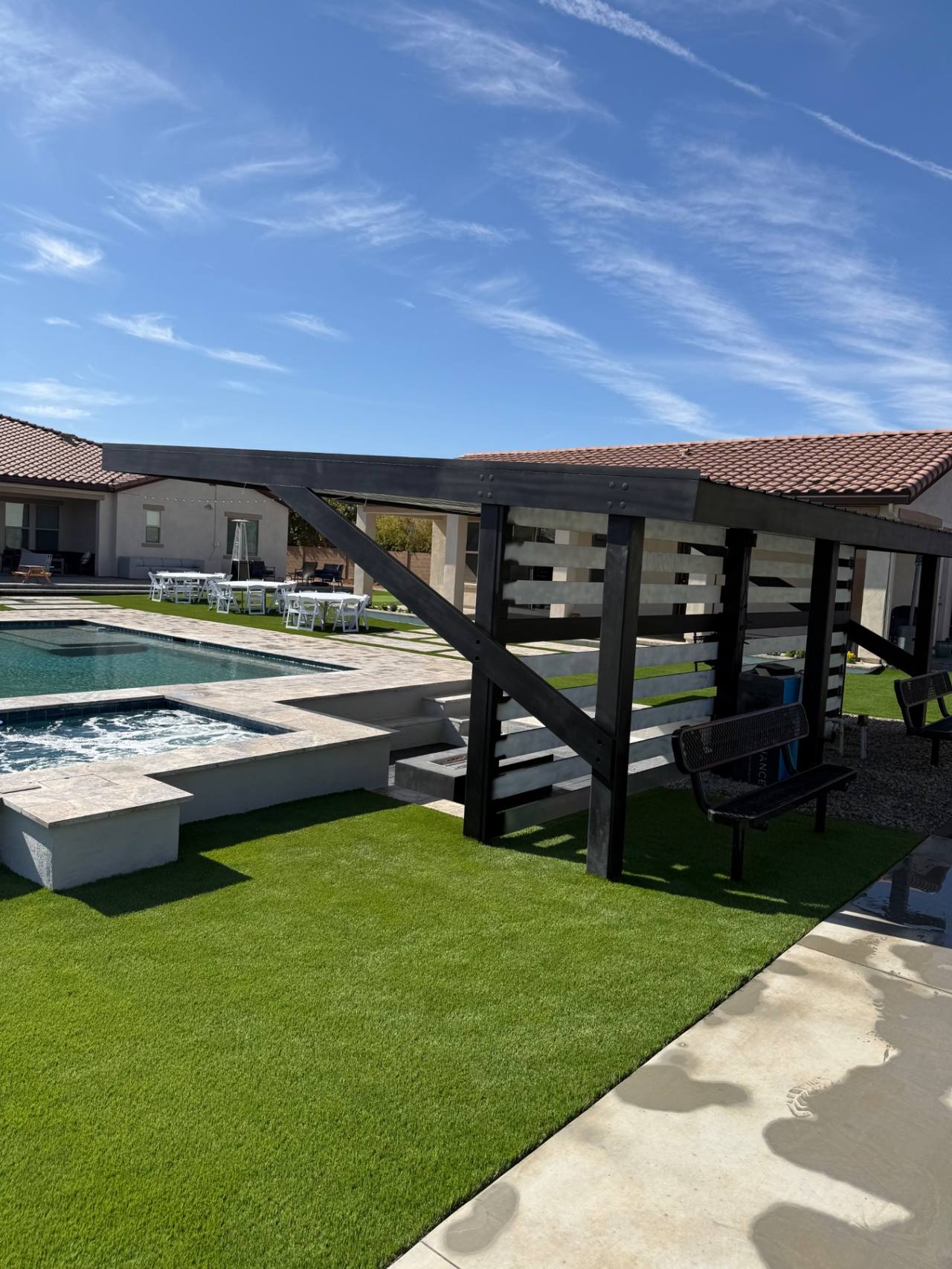 Black steel ramada running alongside a resort-style pool, spa, and turf entertaining lawn.