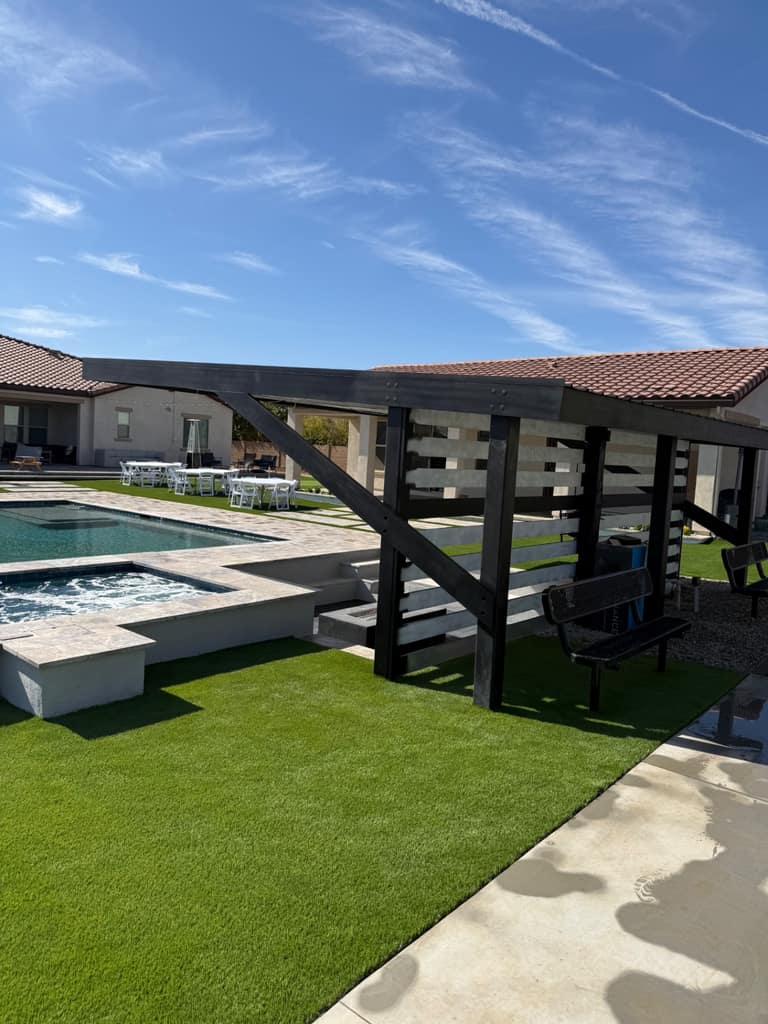 Black steel ramada running alongside a resort-style pool, spa, and turf entertaining lawn.