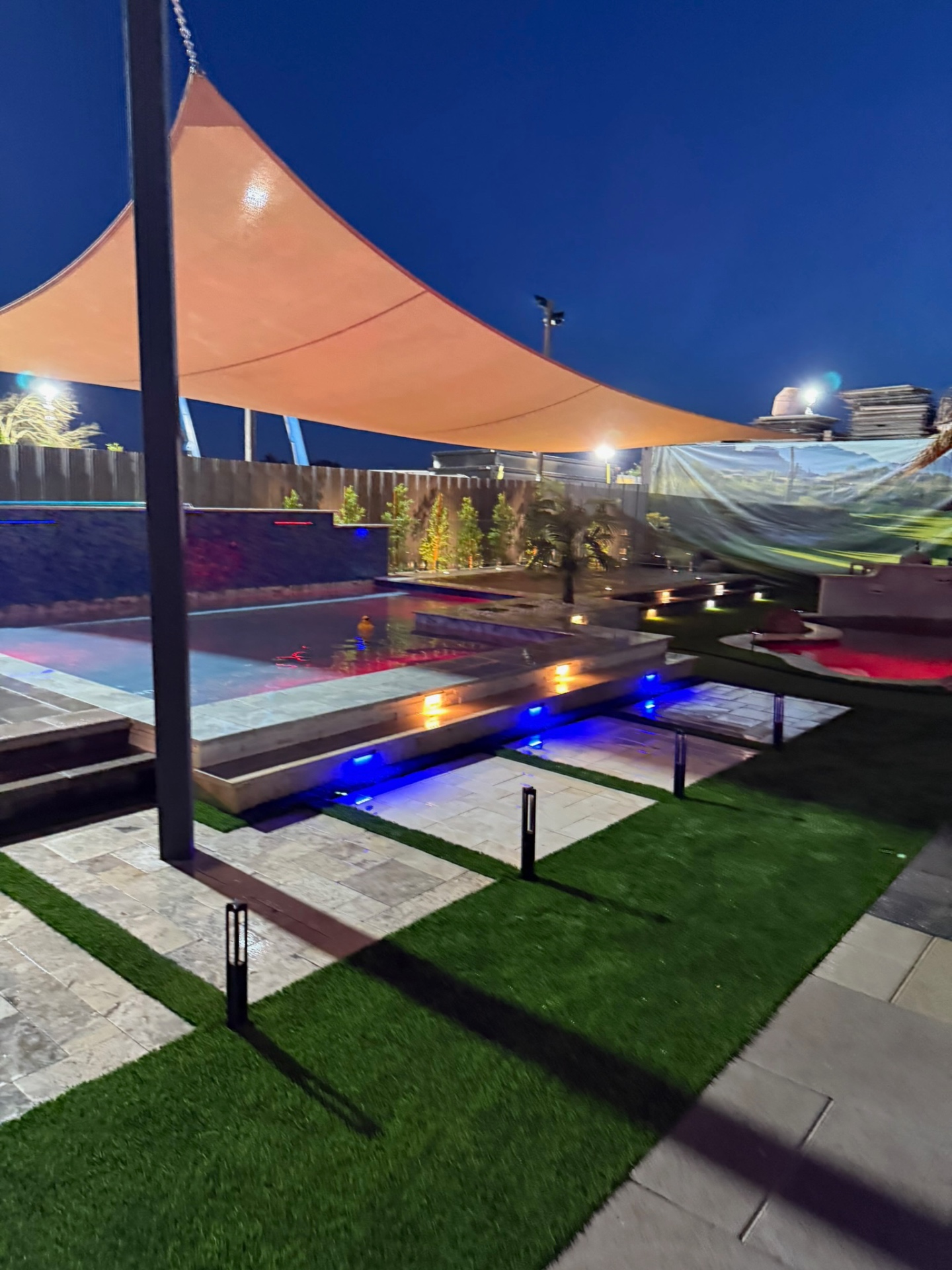 Sail-shaded display pool with warm and blue LED lighting at dusk