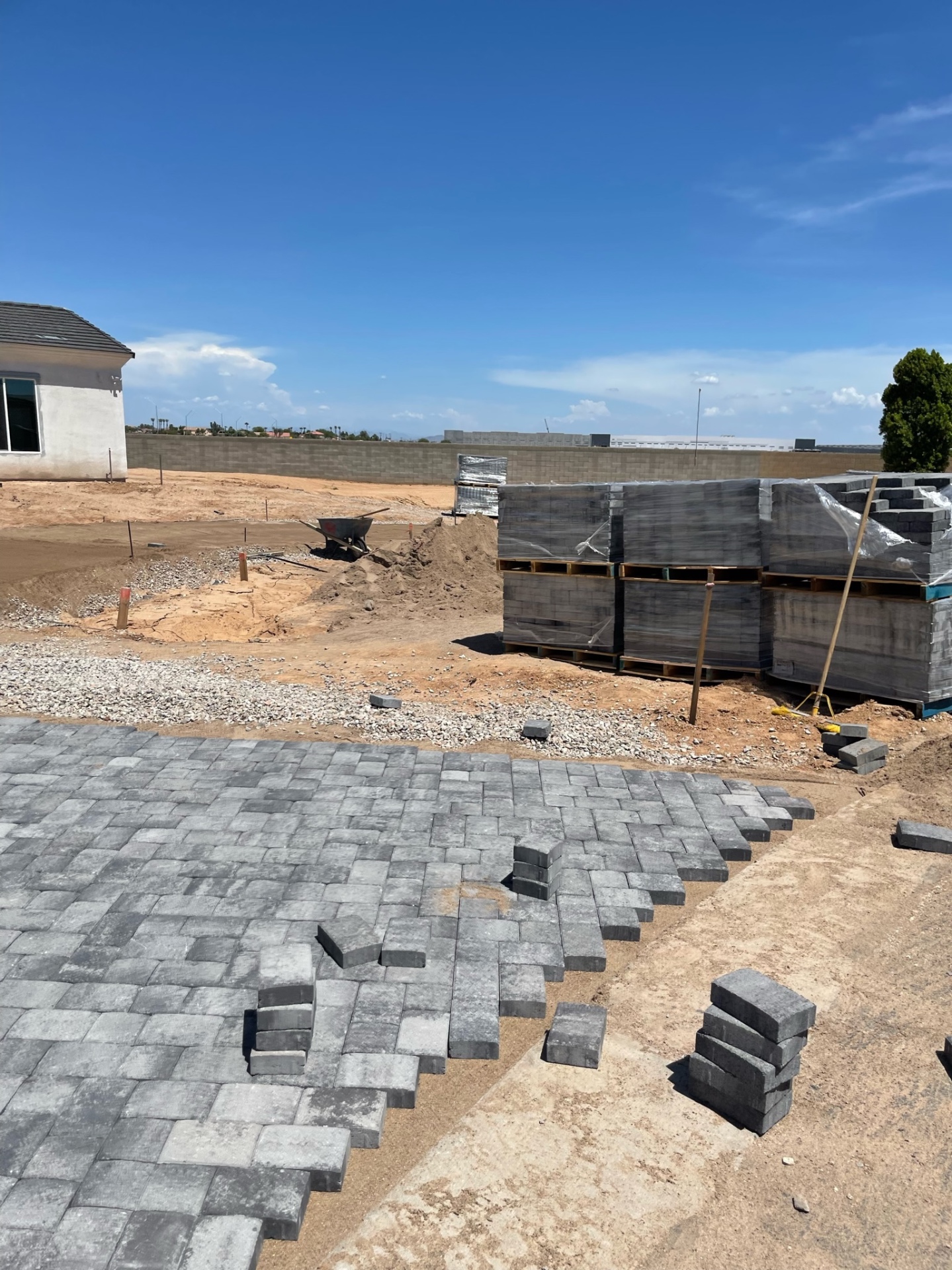 Waddell (Surprise-area) side-yard paver run with staged charcoal-blend paver pallets against block boundary wall on a large custom-home lot by AE Outdoor Living