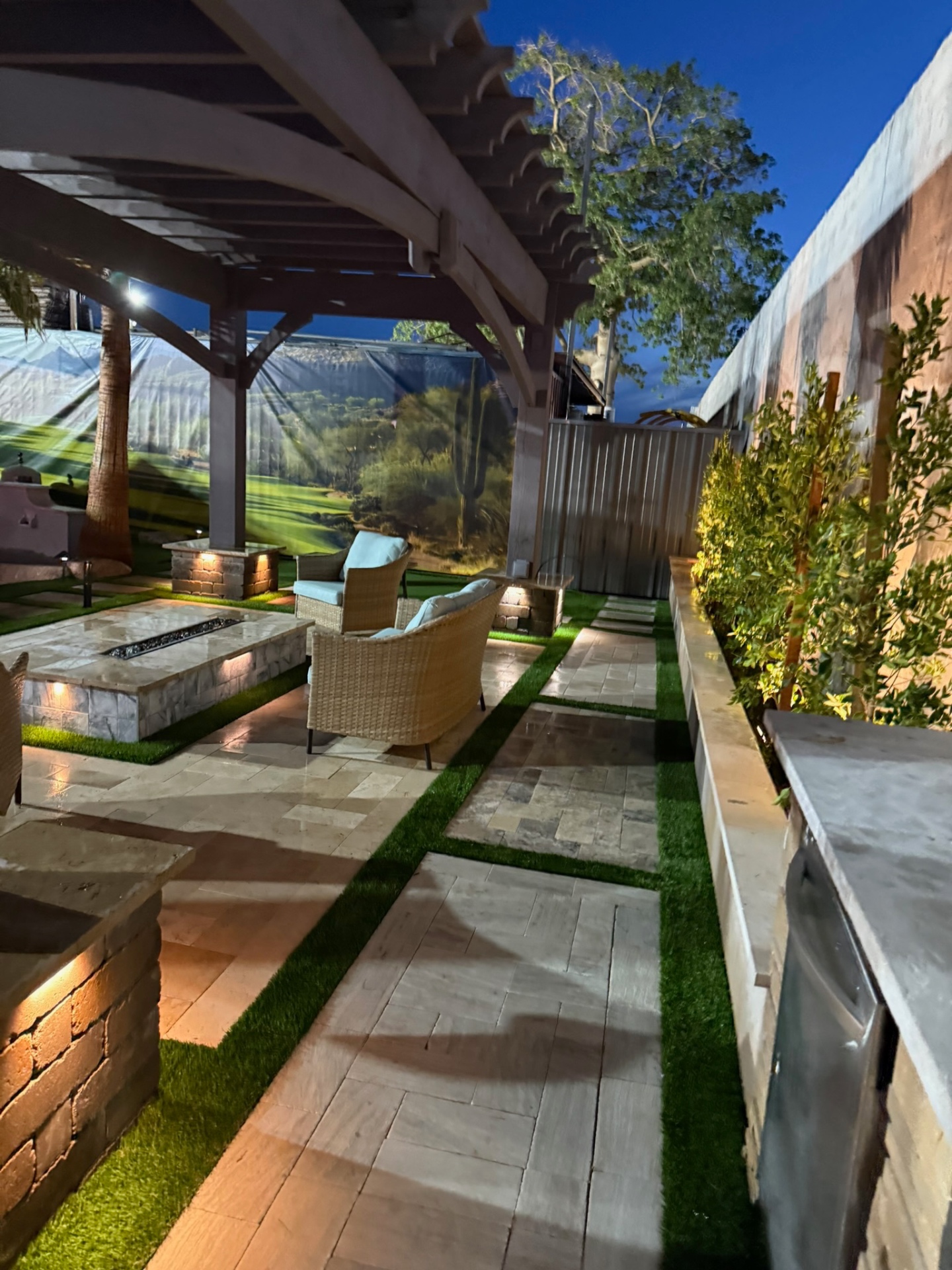 Pergola lounge with stone fire pit, wicker seating, and travertine-and-turf flooring