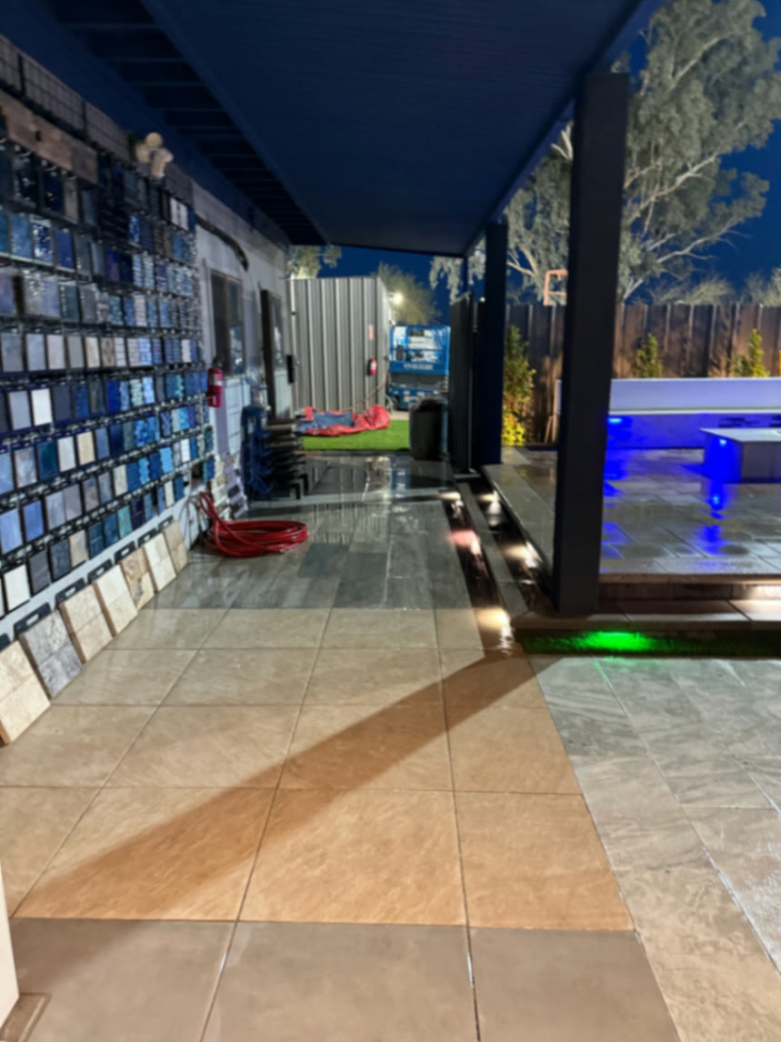 Covered tile sample wall and walkway beside the lit pool display, showing real finish options at night