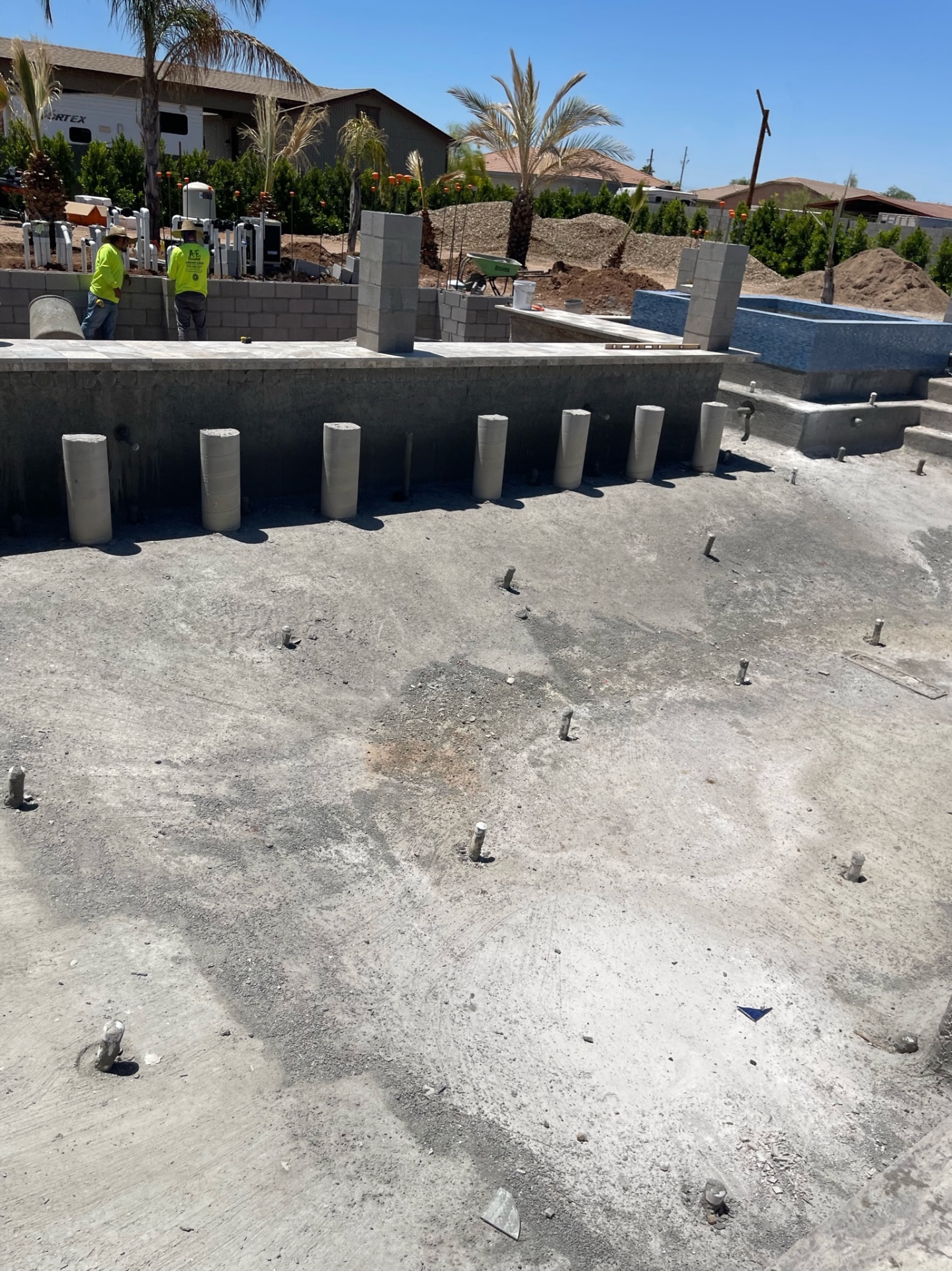 Two AE crew members at the raised wall and pool shell with plumbing manifold and tiled spa visible across the yard