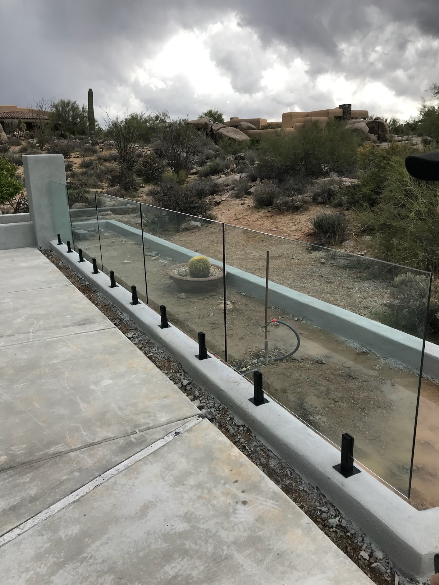 Frameless glass pool barrier viewed from the deck side — clean sightlines through tempered glass to the natural Sonoran landscape.