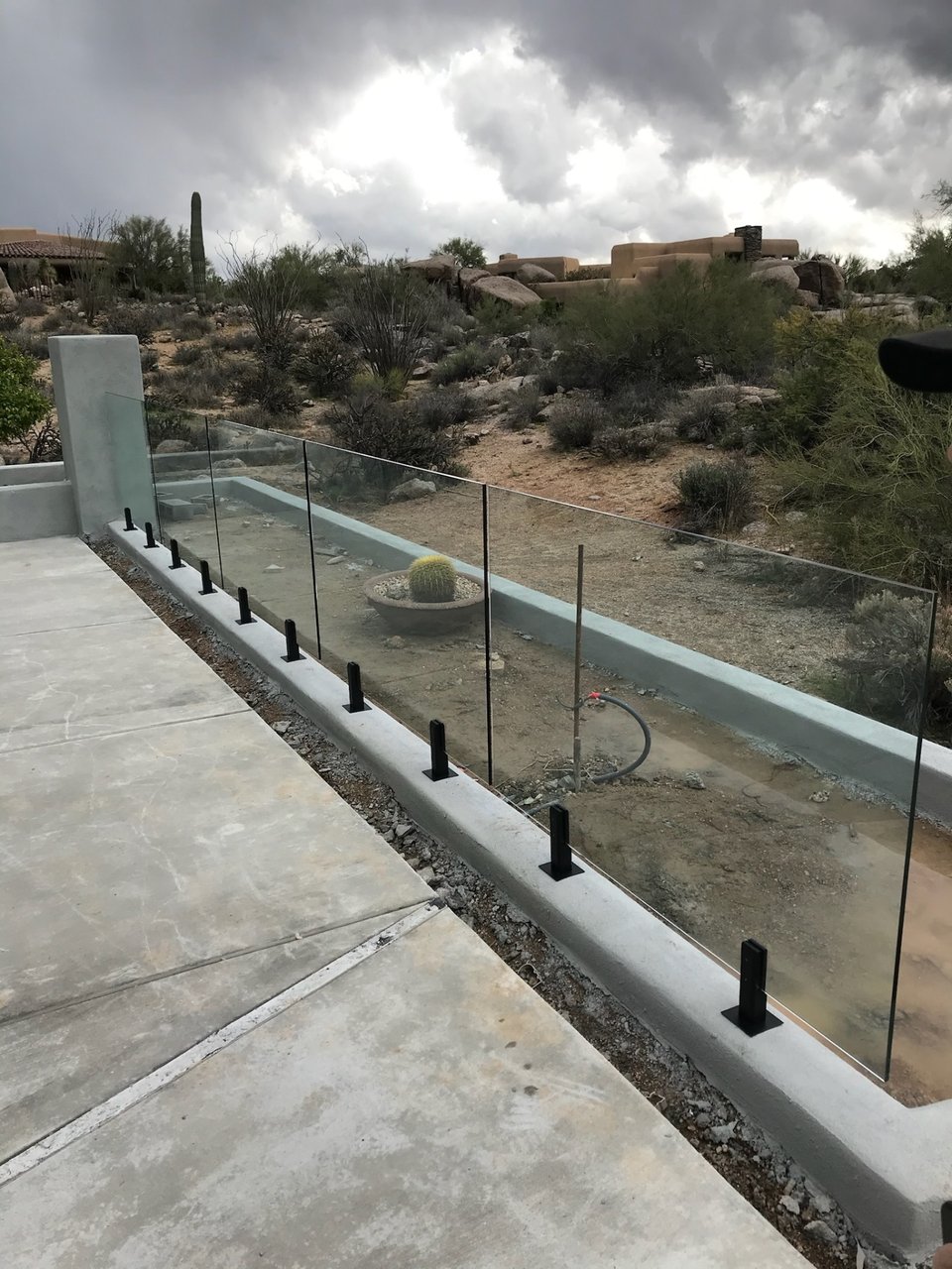 Frameless glass fence viewed from the deck side, with open sightlines through the panels to the surrounding Sonoran Desert landscape.
