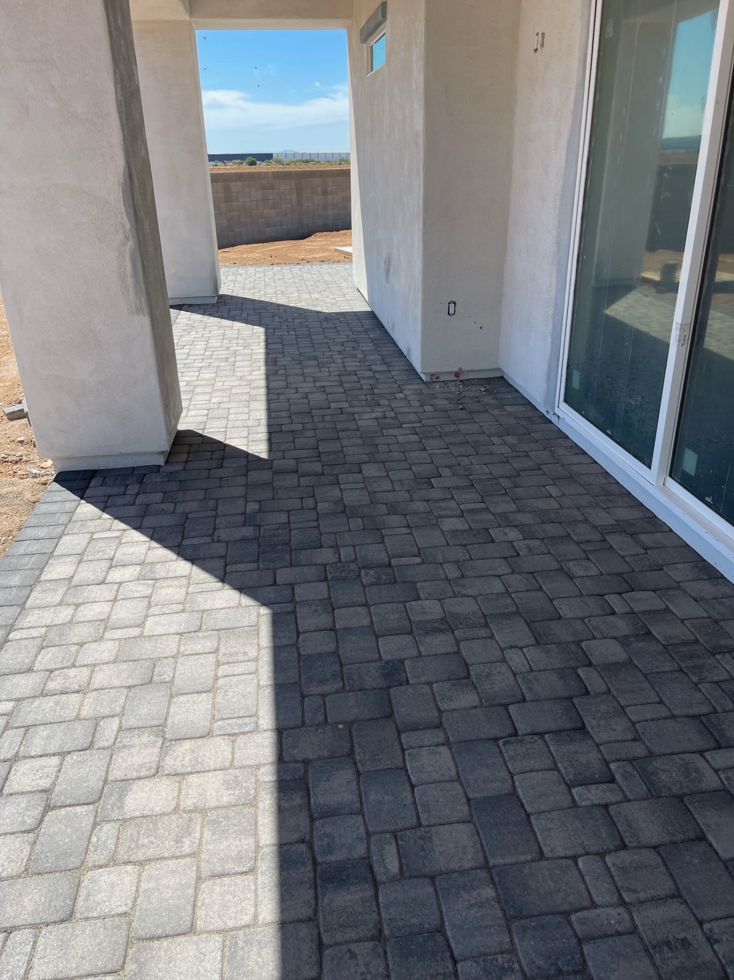 Waddell (Surprise-area) rear covered patio with two-tone charcoal and grey tumbled pavers laid tight to the sliding glass door and stucco wall by AE Outdoor Living