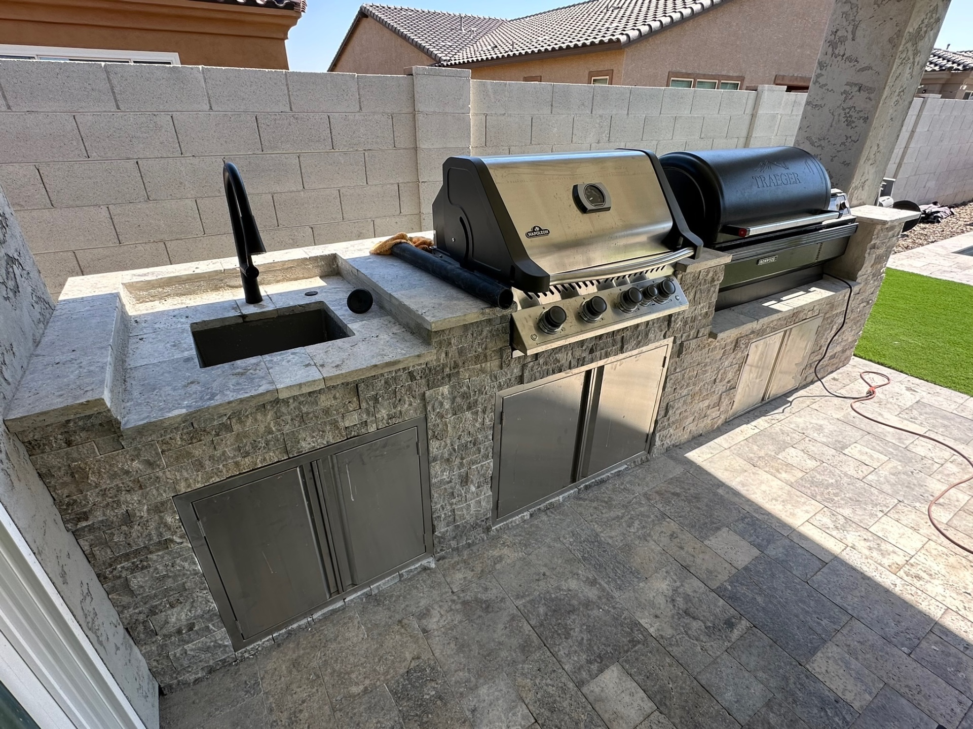 Built-in outdoor kitchen with BBQ island, stone veneer, counter, storage, and low-voltage lighting