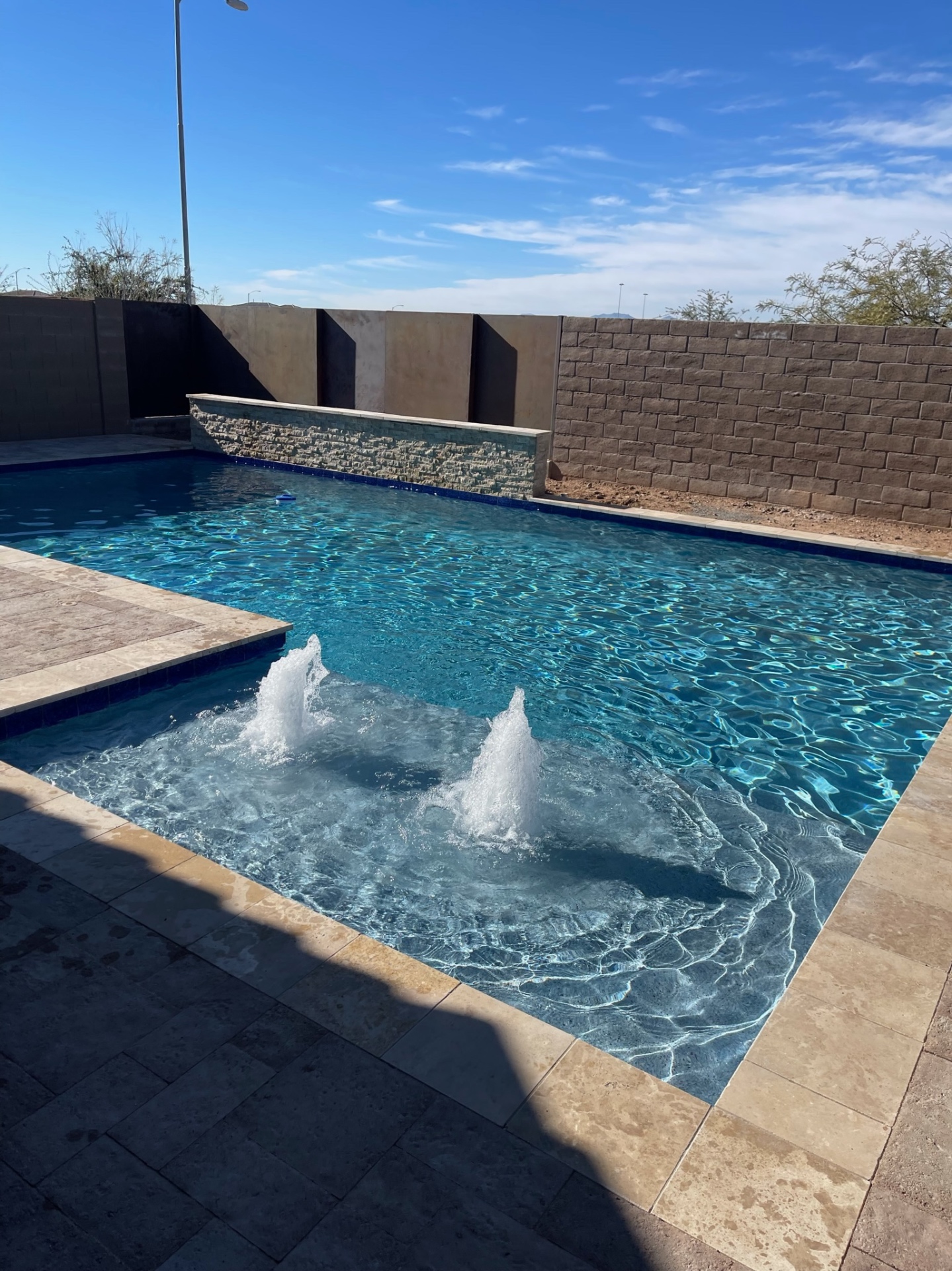 Peoria custom geometric pool with stacked-stone raised water feature wall, blue-glass waterline tile, twin bubbler deck jets and travertine paver deck by AE Outdoor Living