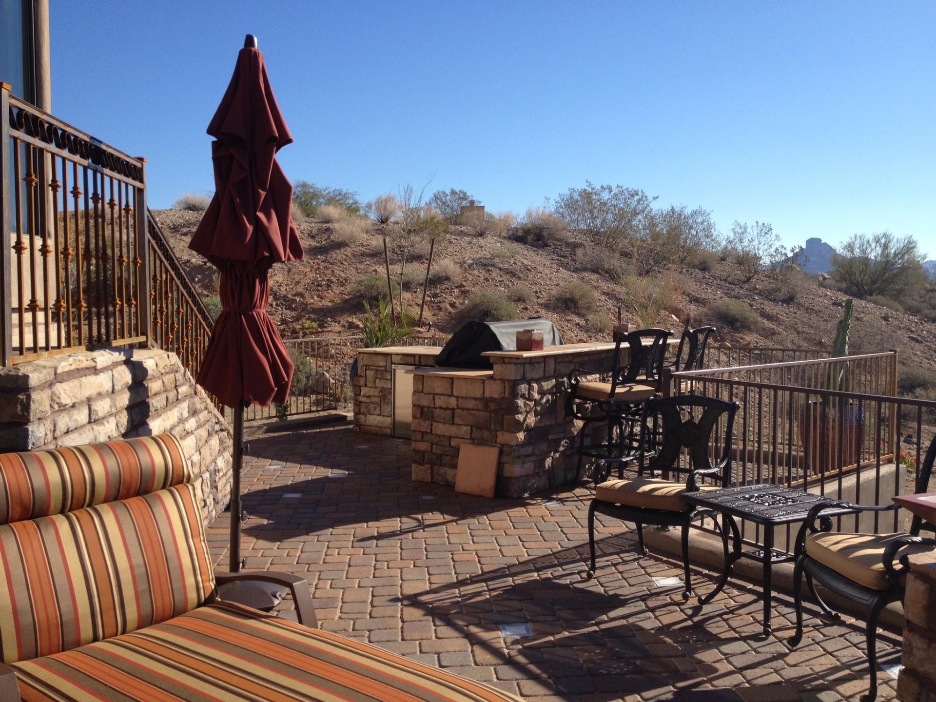 Fountain Hills paver patio with stacked-stone built-in BBQ island, travertine bar counter and wrought-iron view fencing over open desert