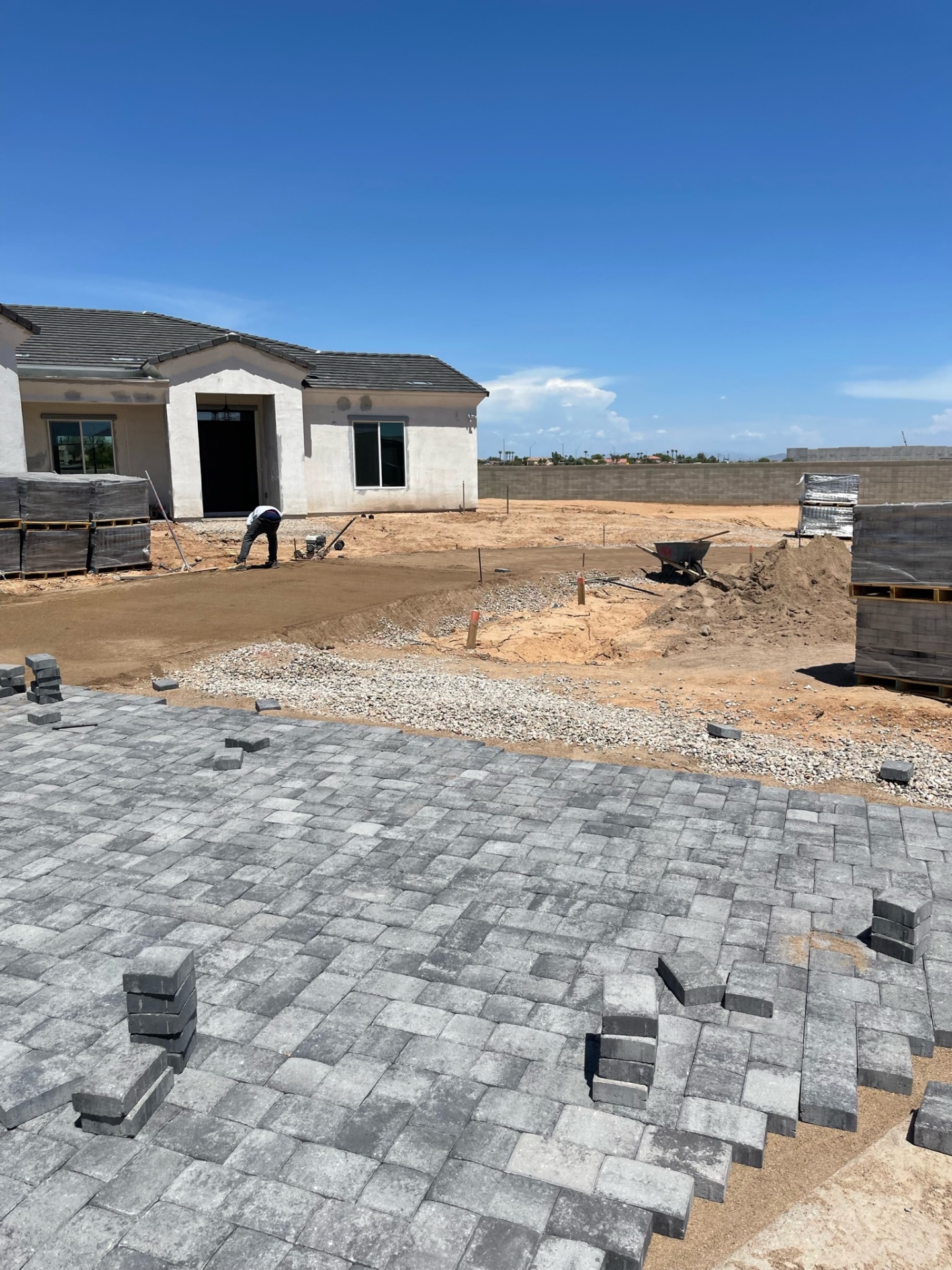 Waddell (Surprise-area) large paver field laid on sand base at front-yard courtyard with cut soldier course curving around planter, painted CMU perimeter wall behind