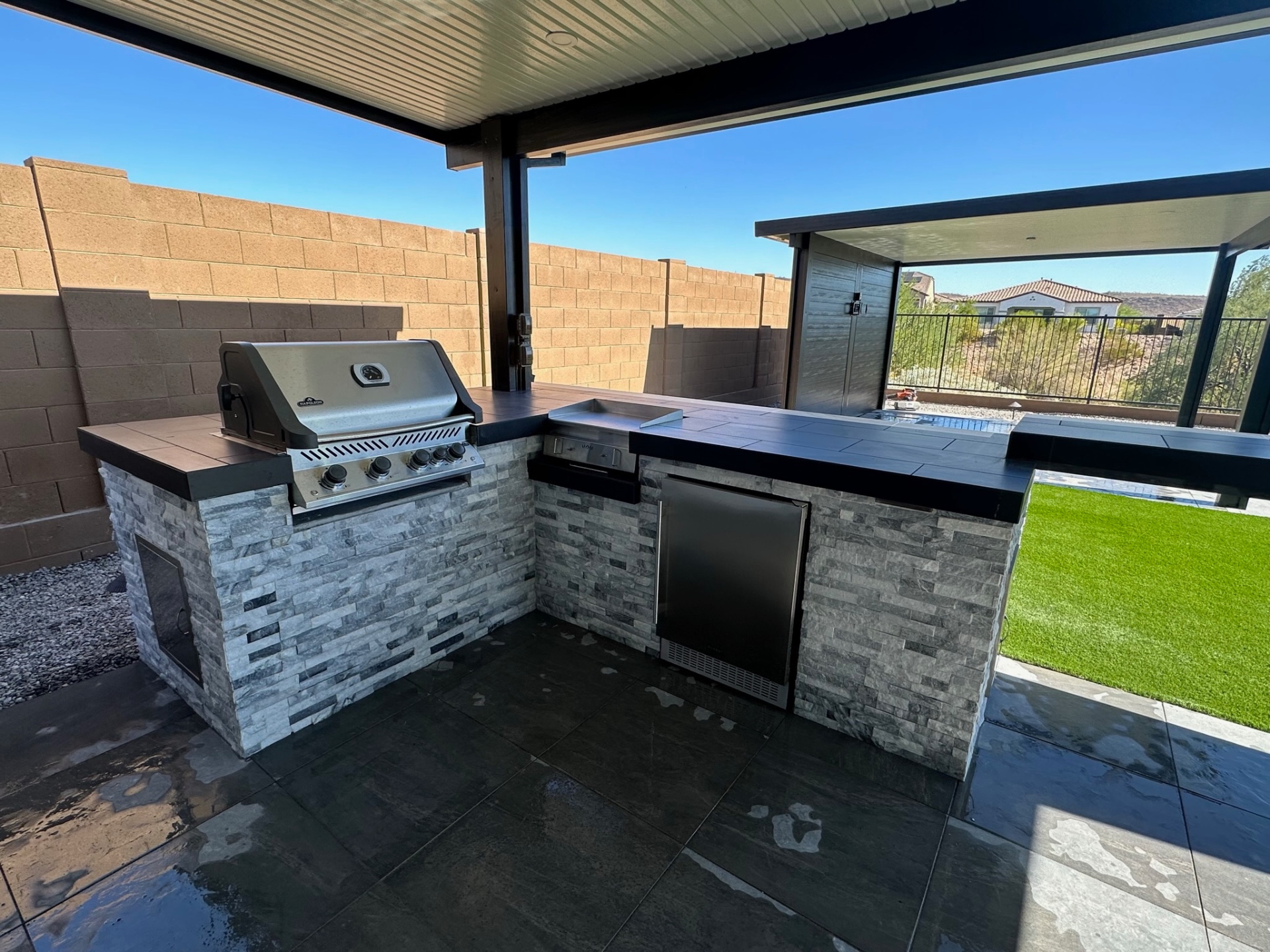 Built-in outdoor kitchen with BBQ island, stone veneer, counter, storage, and low-voltage lighting