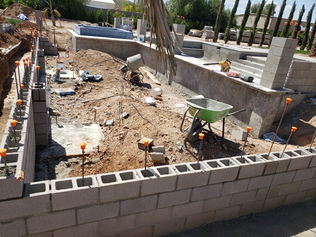 Excavated pool area with raised spa wall built and plumbing trenched, wheelbarrow on site