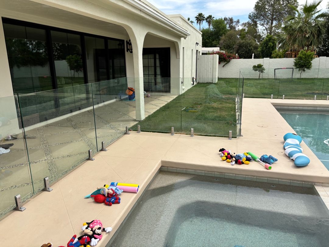 Wide backyard view of a pool and frameless glass barrier with visible panel-top height variation.