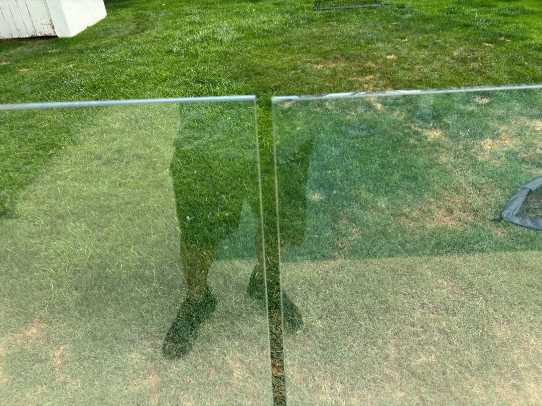 Vertical joint between two frameless glass panels with a visible top-edge offset.
