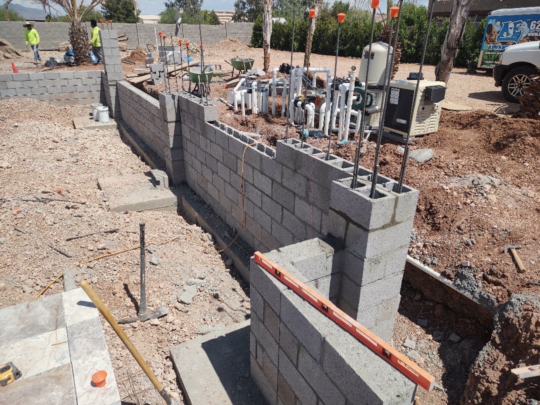 Pool equipment pad with plumbed PVC manifold, pumps and filter beside in-progress block wall