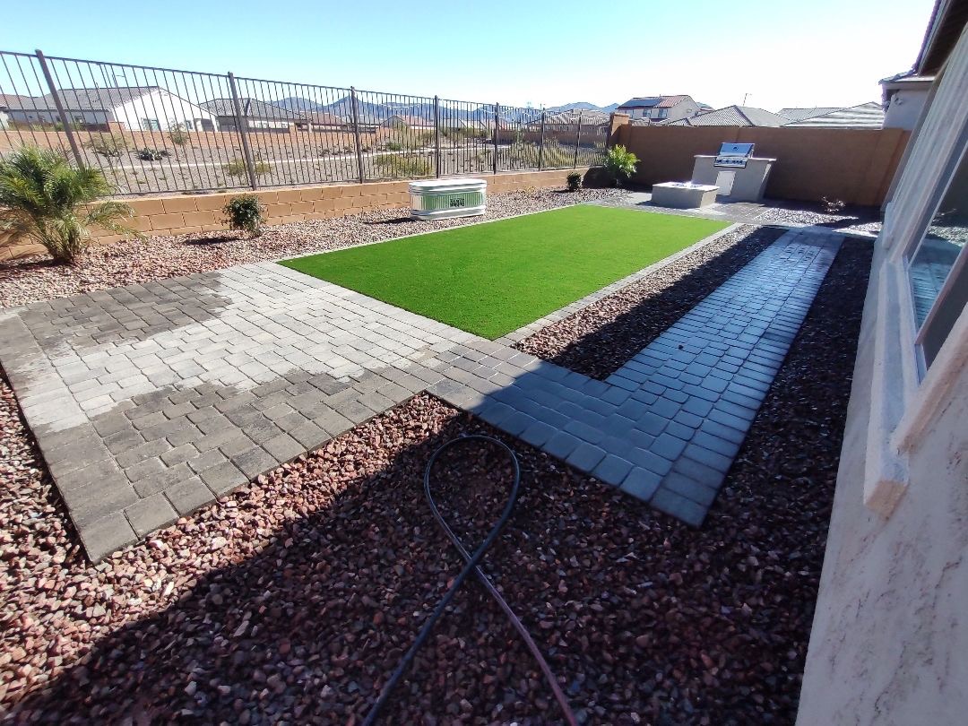 Vistancia (Peoria) backyard layout with charcoal paver patio, artificial turf lawn, stucco outdoor kitchen and stock-tank spa framed by wrought-iron view fencing to McDowell Mountain foothills by AE Outdoor Living